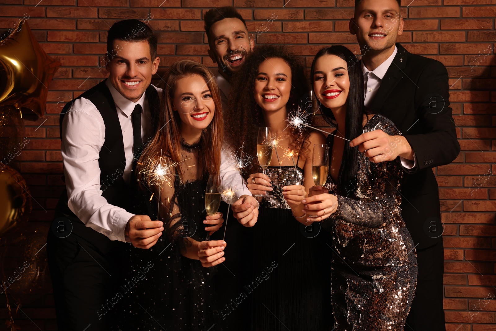 Photo of Happy friends with glasses of sparkling wine and sparklers celebrating New Year indoors