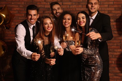 Happy friends with glasses of sparkling wine and sparklers celebrating New Year indoors