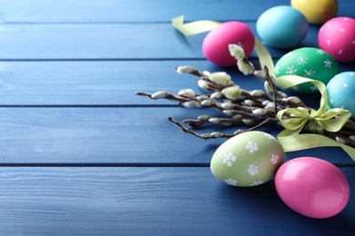 Photo of Bright painted eggs and pussy willows on blue wooden table, space for text. Happy Easter