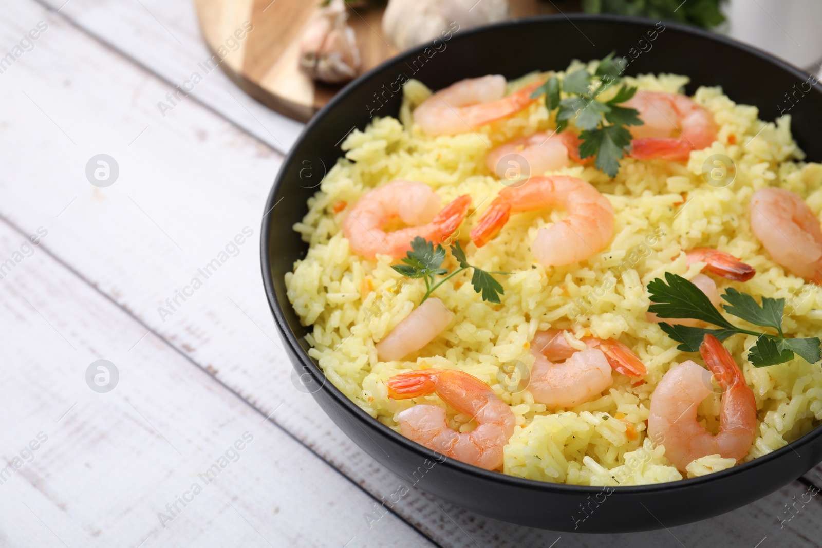 Photo of Delicious risotto with shrimps and parsley in bowl on white wooden table, closeup. Space for text