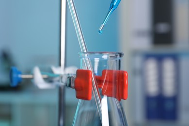 Photo of Laboratory analysis. Dripping blue liquid into flask on stand indoors, closeup