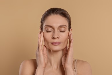 Woman massaging her face on beige background