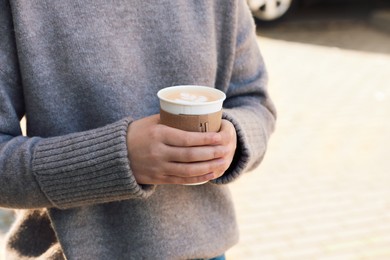 Photo of Woman holding takeaway cardboard cup on city street, closeup. Coffee to go