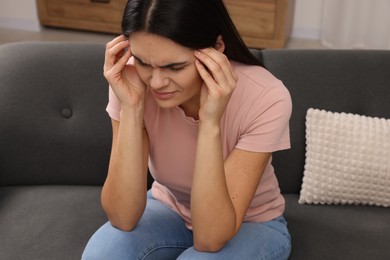 Photo of Sad woman suffering from headache on sofa indoors