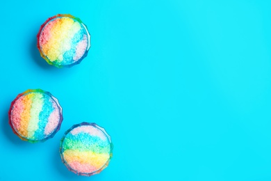 Photo of Rainbow shaving ice in glass dessert bowls on light blue background, flat lay. Space for text