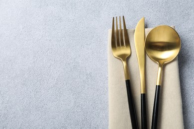 Stylish golden cutlery and napkin on grey table, top view. Space for text