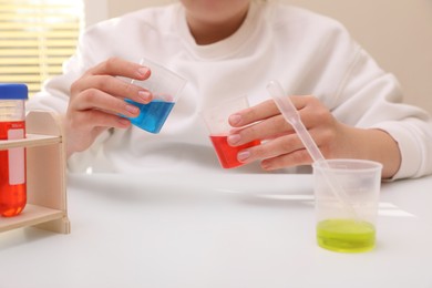 Photo of Girl mixing colorful liquids at white table indoors, closeup. Chemical experiment set for kids