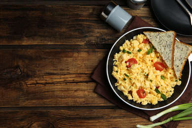 Photo of Tasty scrambled eggs served on wooden table, flat lay. Space for text