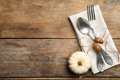 Autumn table setting, space for text. Cutlery with napkin, acorns and white pumpkin on wooden background, flat lay