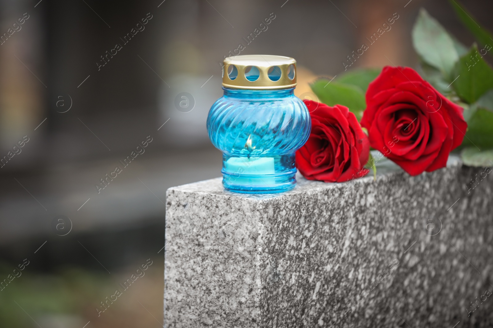 Photo of Red roses and candle on grey granite tombstone outdoors. Funeral ceremony