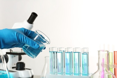 Photo of Scientist pouring liquid from beaker into test tubes on light background, closeup with space for text. Solution chemistry