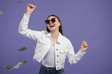 Happy woman under money shower on purple background