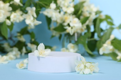 Photo of Presentation of product. White podium and beautiful jasmine flowers on light blue background, closeup. Space for text