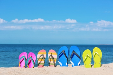 Photo of Composition with bright flip flops on sand near sea in summer. Beach accessories