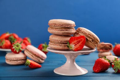 Photo of Delicious macarons and strawberries on blue wooden table