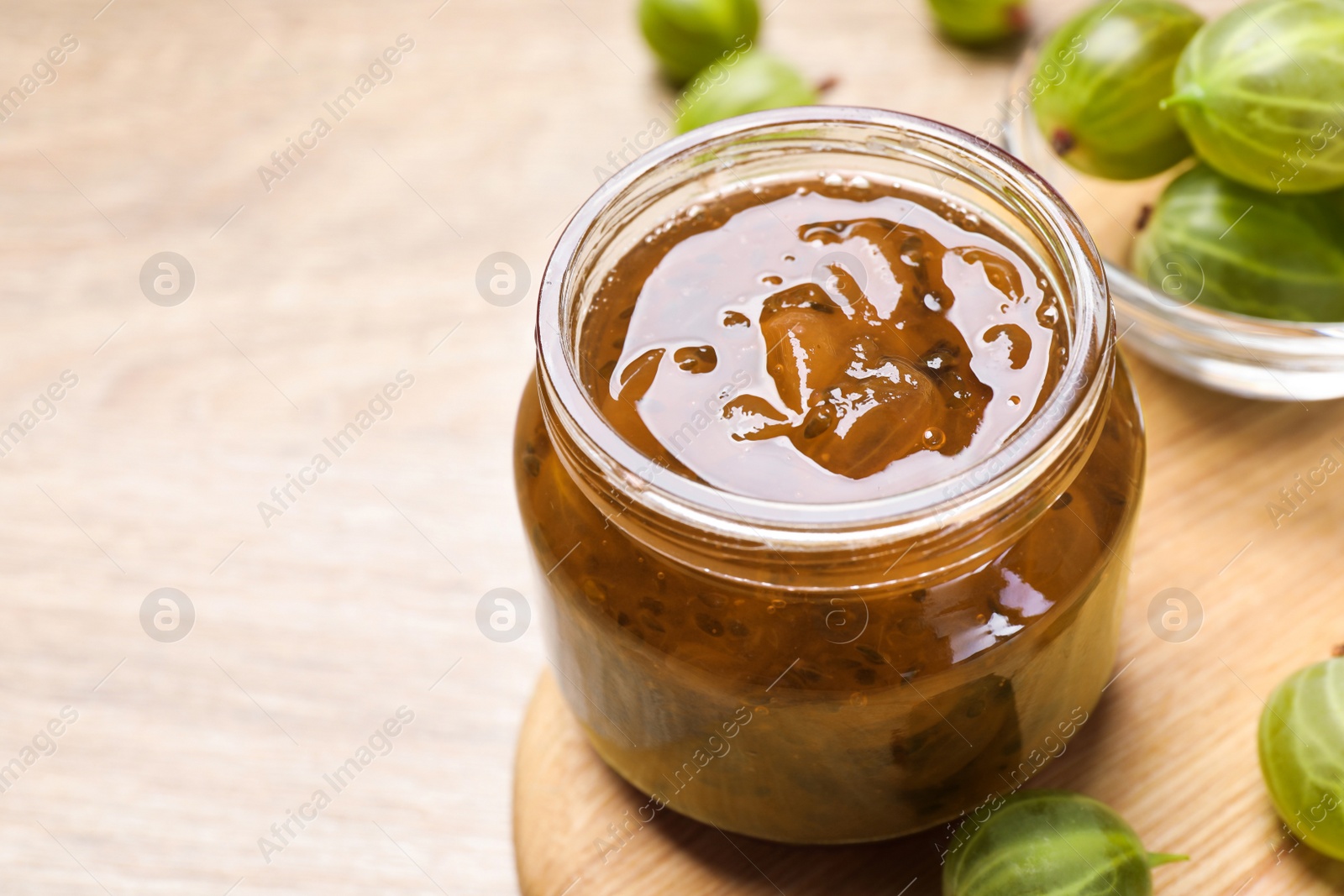 Photo of Jar of delicious gooseberry jam and fresh berries on wooden table, closeup. Space for text