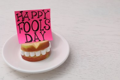 Words Happy Fool's Day and sandwich of apple slices with marshmallows on wooden table. Space for text