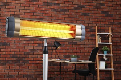 Photo of Electric infrared heater near brick wall in stylish room, closeup