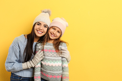 Photo of Happy mother and daughter in warm clothes on yellow background, space for text. Winter vacation