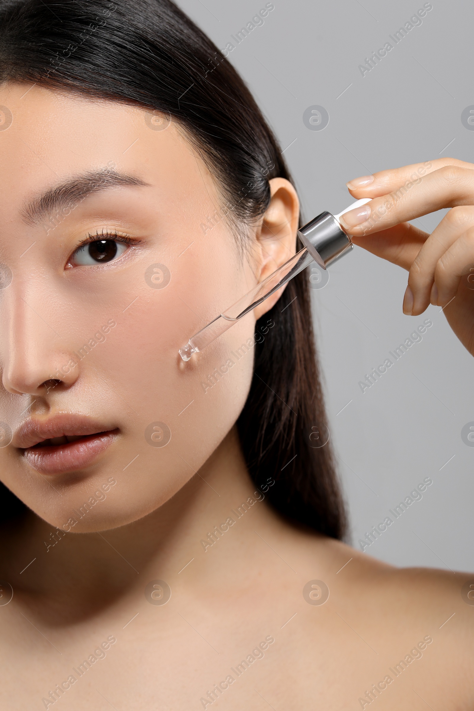 Photo of Beautiful young woman applying cosmetic serum onto her face on grey background