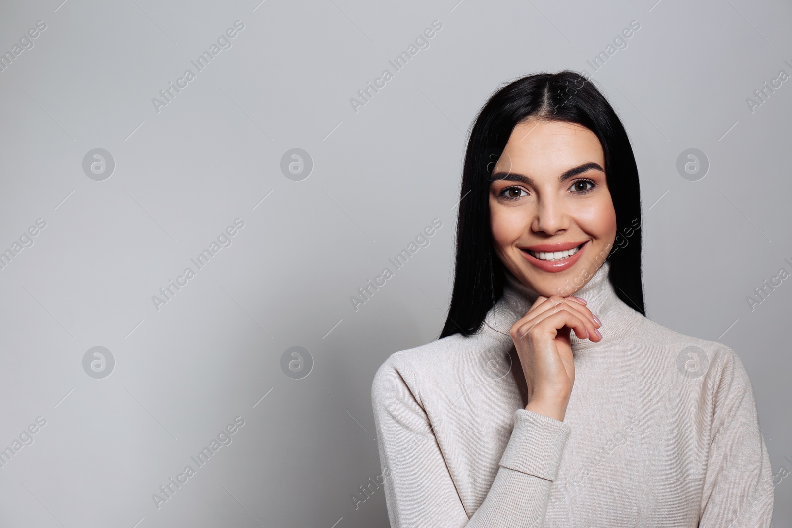 Photo of Portrait of happy young woman with beautiful black hair and charming smile on light grey background, space for text