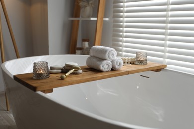 Wooden tray with spa products and burning candles on bath tub in bathroom