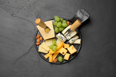Photo of Cheese platter with specialized knife and fork on black table, top view