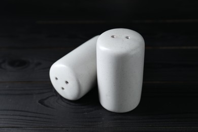 Photo of Pepper and salt shakers on black wooden table, closeup