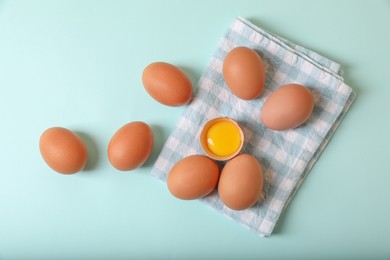 Cracked and whole chicken eggs with napkin on light blue background, flat lay