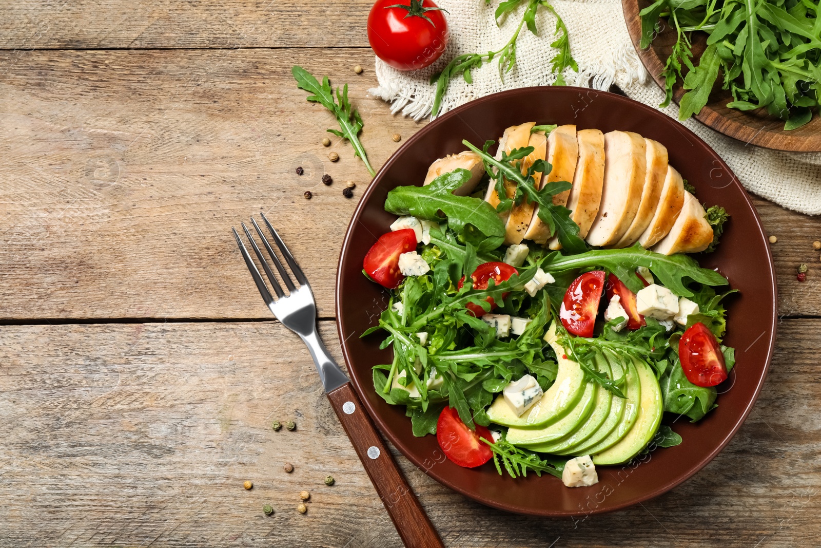 Photo of Delicious salad with chicken, arugula and avocado on wooden table, flat lay. Space for text