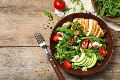 Photo of Delicious salad with chicken, arugula and avocado on wooden table, flat lay. Space for text