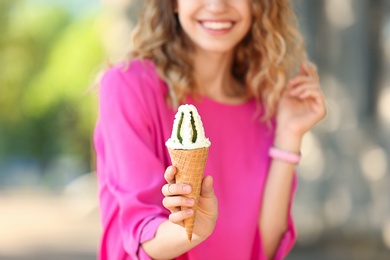 Happy young woman with delicious ice cream in waffle cone outdoors, closeup