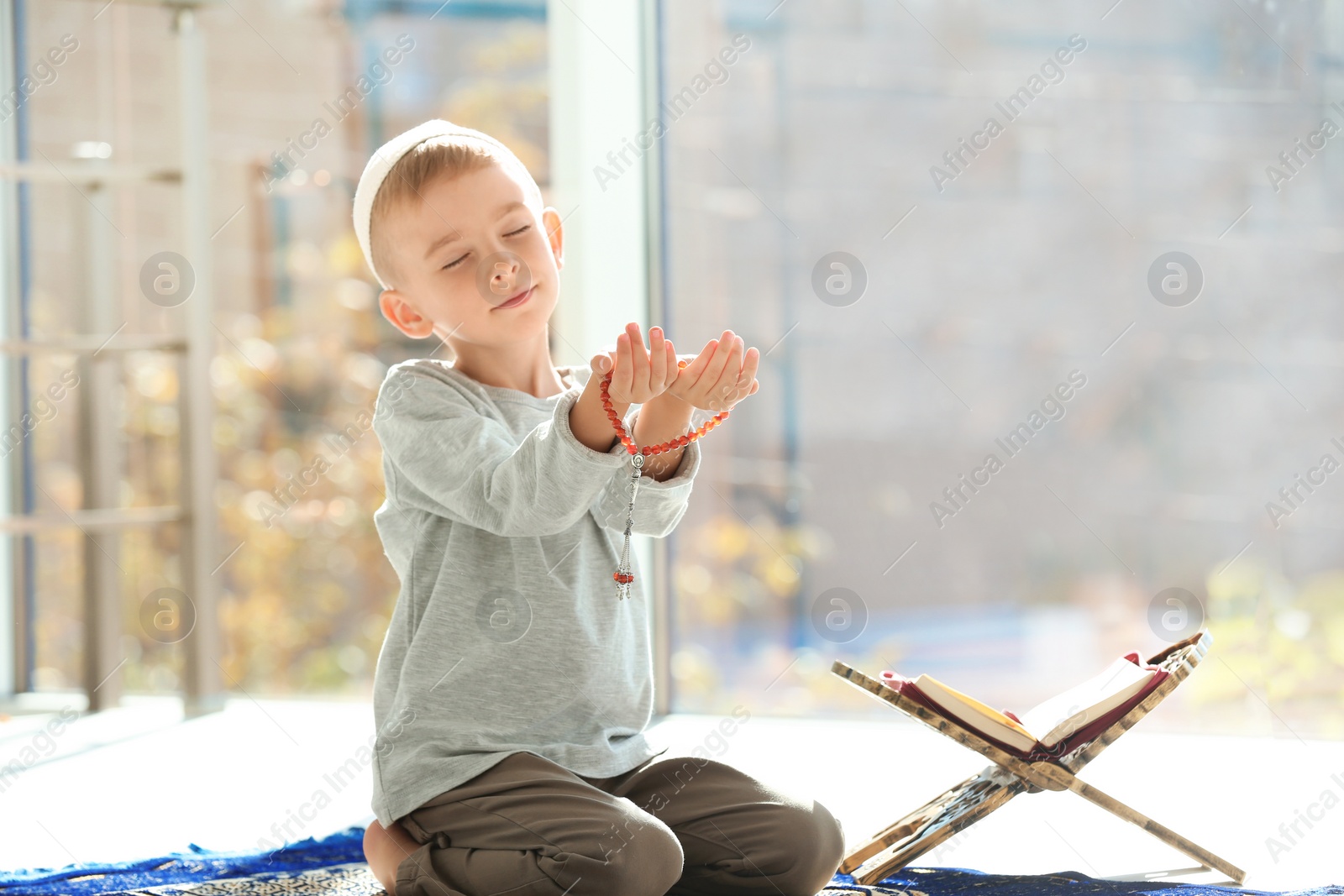 Photo of Little Muslim boy with misbaha and Koran praying on rug indoors