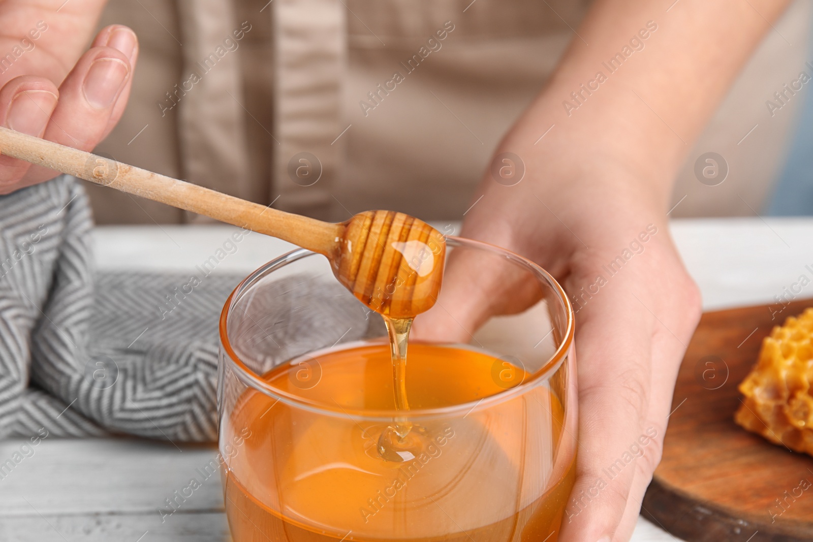 Photo of Woman with honey and dipper at white wooden table, closeup