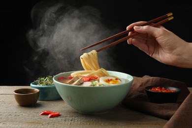 Photo of Woman eating delicious ramen with chopsticks at wooden table, closeup. Noodle soup