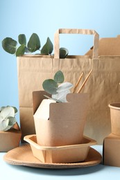 Photo of Eco friendly food packaging. Paper containers, tableware, bag and eucalyptus branches on white table against light blue background