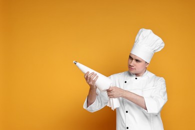 Photo of Portrait of confectioner in uniform holding piping bag on orange background, space for text