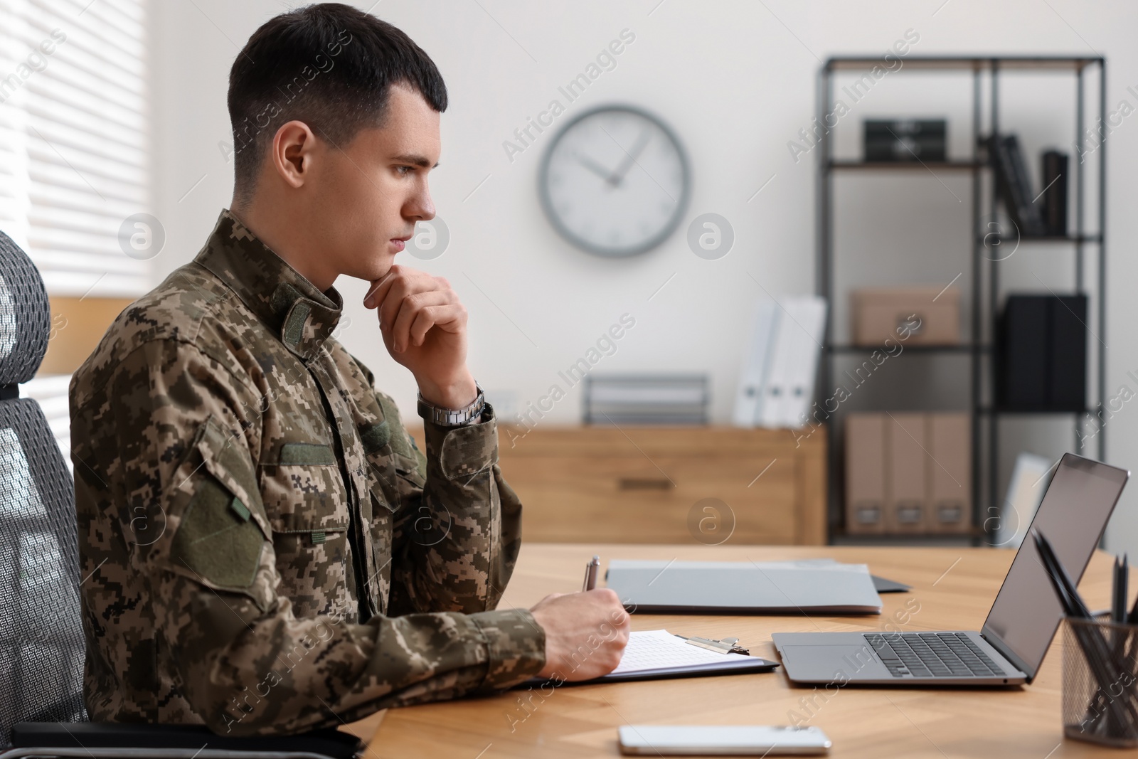 Photo of Military service. Young soldier working at wooden table in office