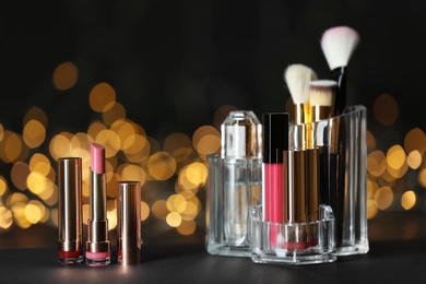 Photo of Bright lipsticks and holder with other makeup products on table against blurred lights