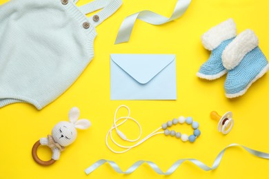 Photo of Envelope for baby shower, clothes and accessories on turquoise background, flat lay