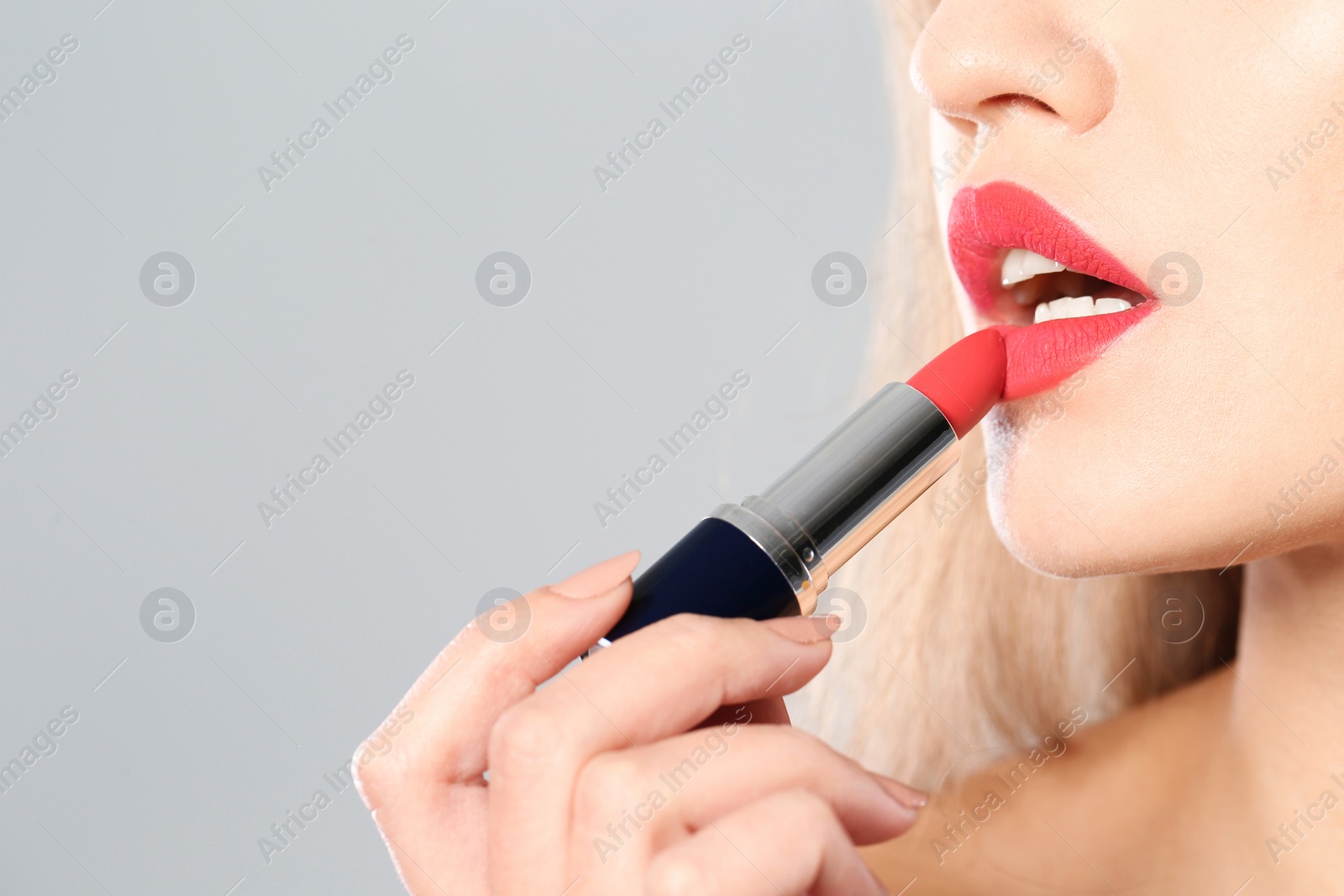 Photo of Young woman applying red lipstick on gray background, closeup. Space for text