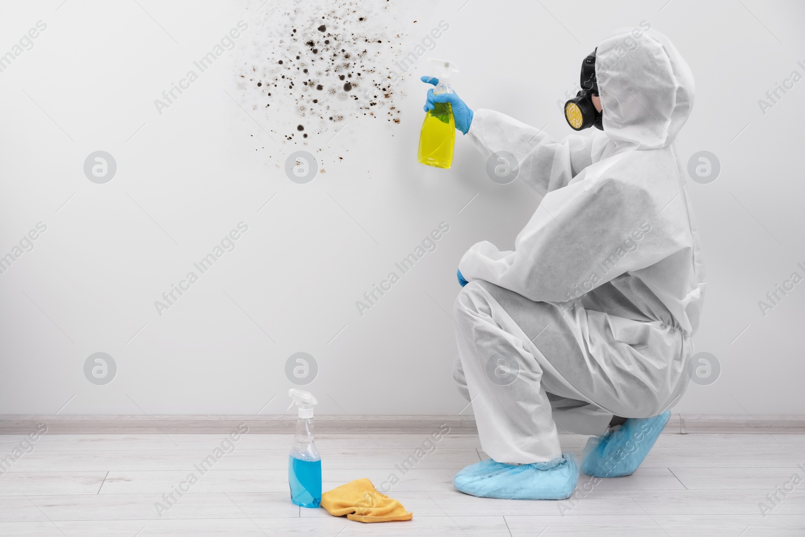 Image of Woman in protective suit and rubber gloves using mold remover on wall