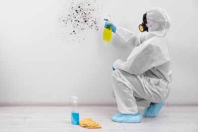 Woman in protective suit and rubber gloves using mold remover on wall