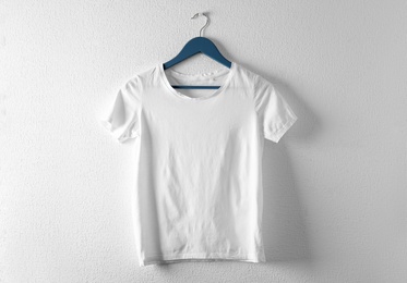 Photo of Hanger with white t-shirt on light background. Mockup for design