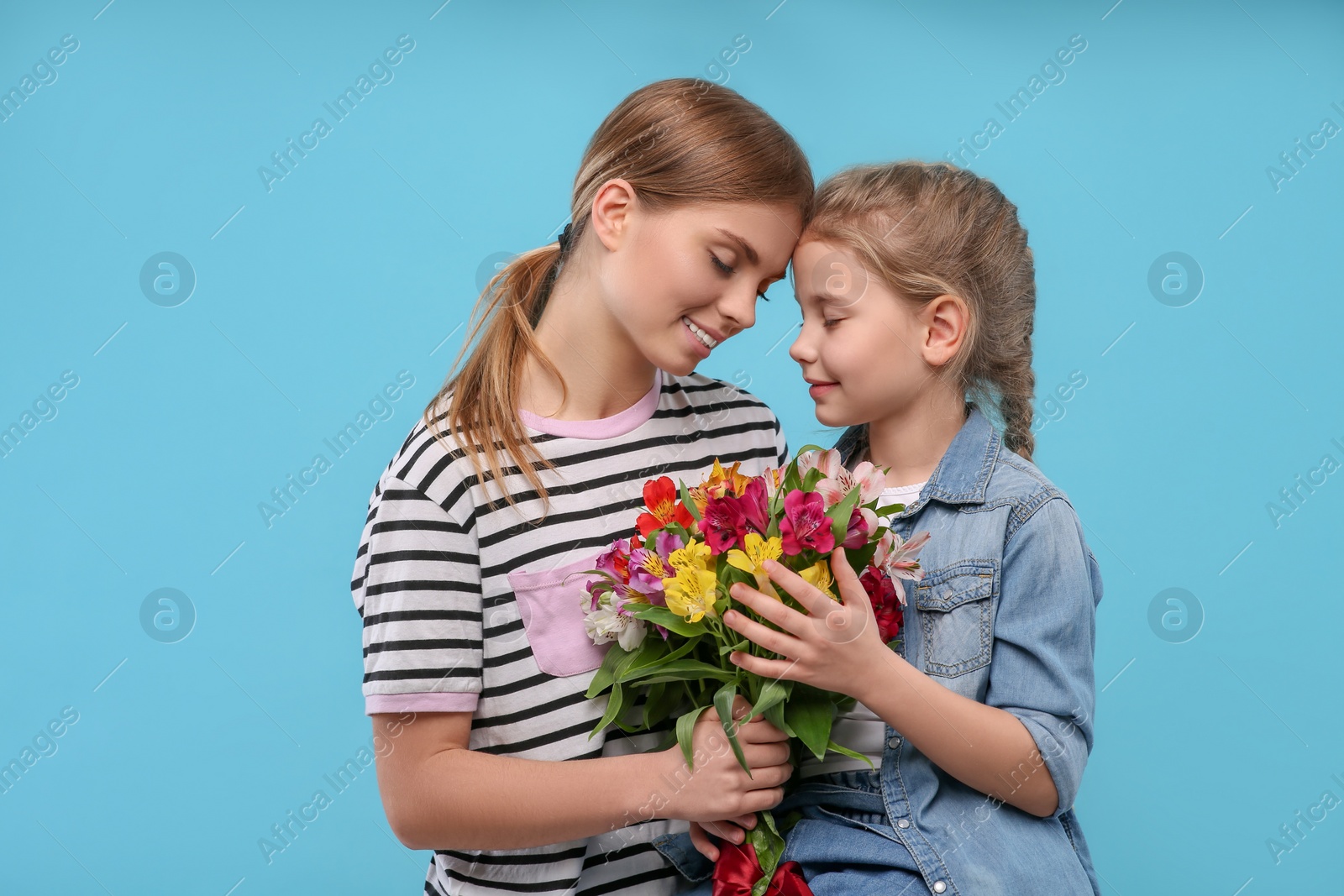 Photo of Little daughter congratulating her mom with flowers on light blue background. Happy Mother's Day