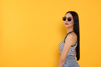 Photo of Attractive serious woman in fashionable sunglasses against orange background. Space for text