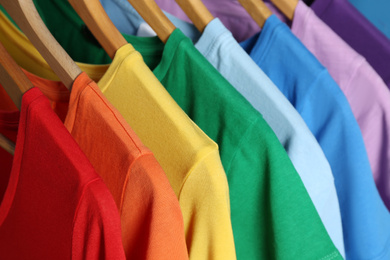 Bright clothes on wooden hangers, closeup. Rainbow colors