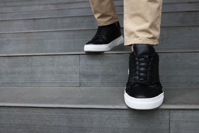 Photo of Man in stylish black leather sneakers walking down stairs, closeup. Space for text