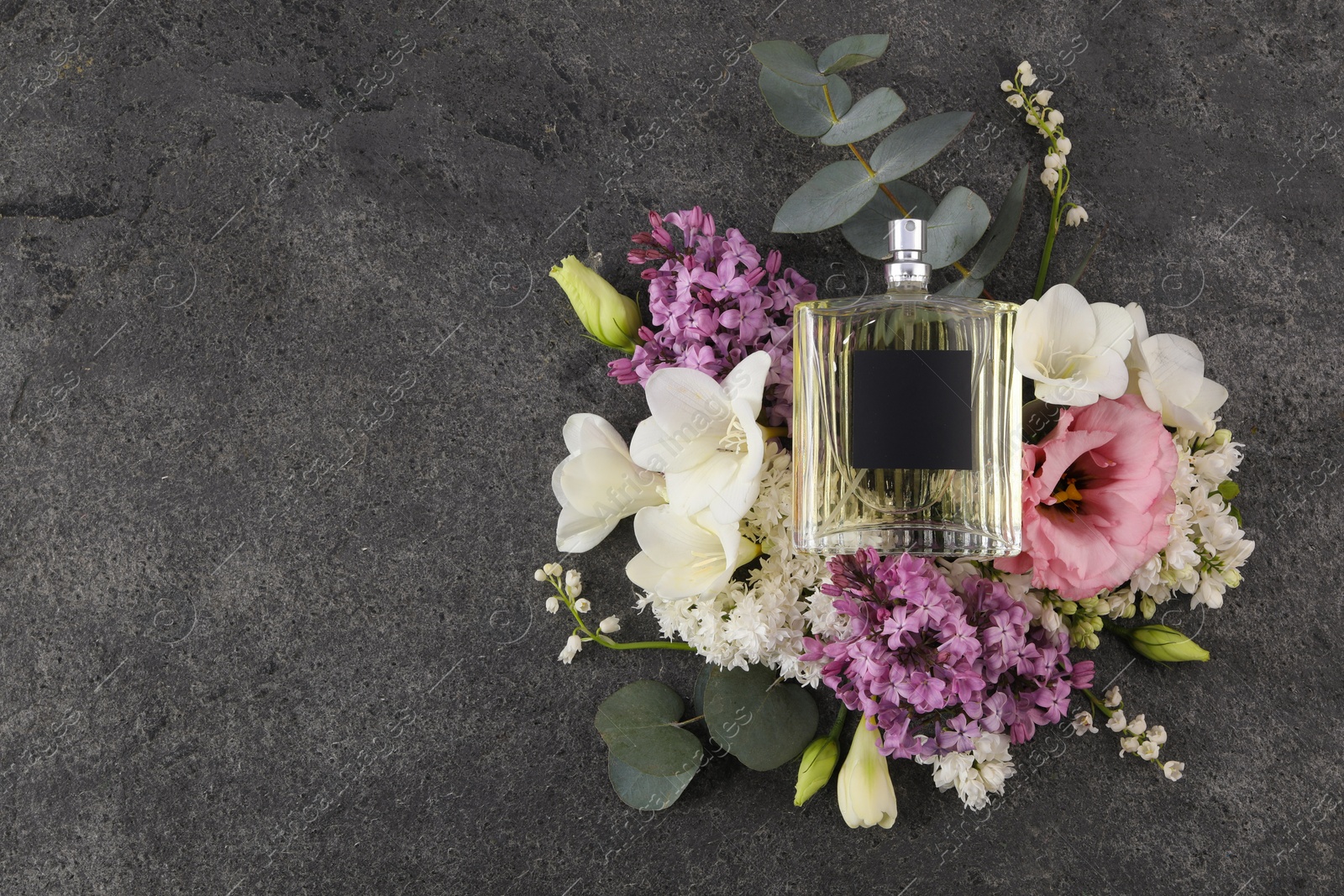 Photo of Bottle of luxury perfume and floral decor on dark grey table, top view. Space for text