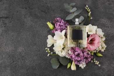 Photo of Bottle of luxury perfume and floral decor on dark grey table, top view. Space for text